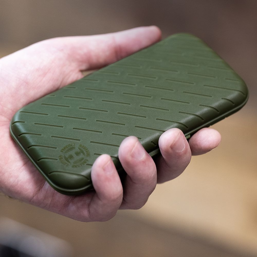 Estuche para dardos Harrows Slimcase Eine Hand hält ein schlankes, grünes Etui. Das Etui hat ein strukturiertes Muster und ein rundes Logo in der Ecke.