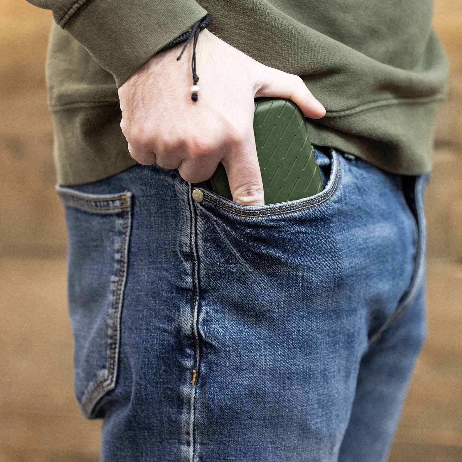 Estuche para dardos Harrows Slimcase Eine Person steckt ein grünes Etui in die vordere Hosentasche einer Jeans. Das Etui hat eine strukturierte Oberfläche und passt gut in die Tasche.