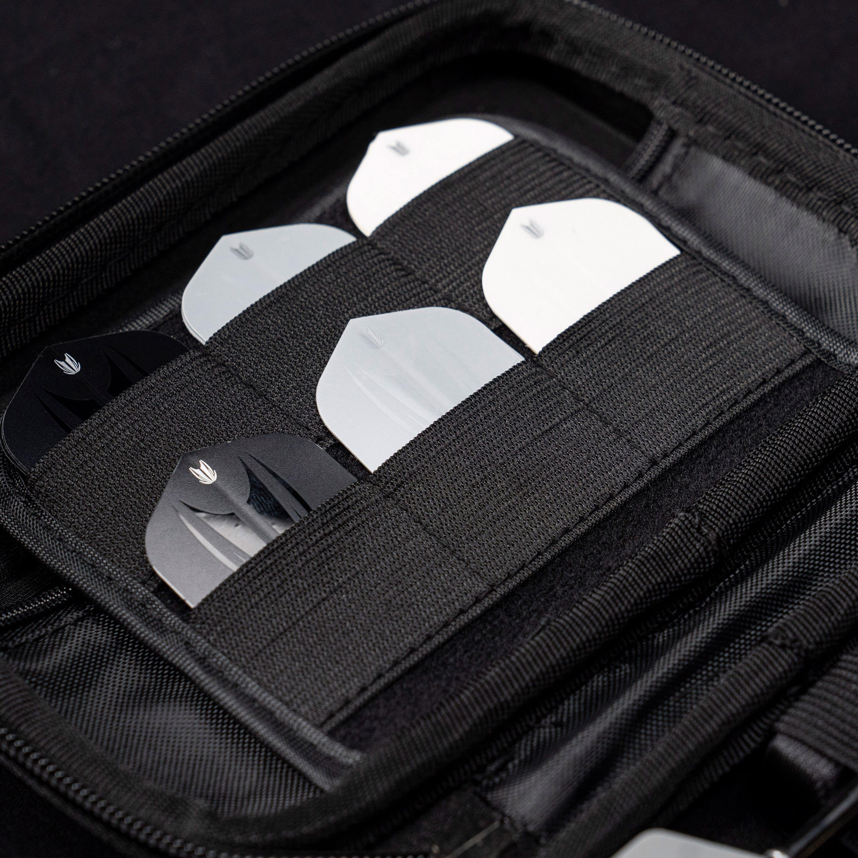 Estuche de dardos Chris Dobey de la serie Ghost de Takoma XL Das Bild zeigt das „Target Takoma Bolide XL Dartcase“, das mehrere Dart-Flights in schwarzen und weißen Farben organisiert aufbewahrt. Die Flights sind sicher in elastischen Halterungen im Inneren des schwarzen Etuis verstaut.