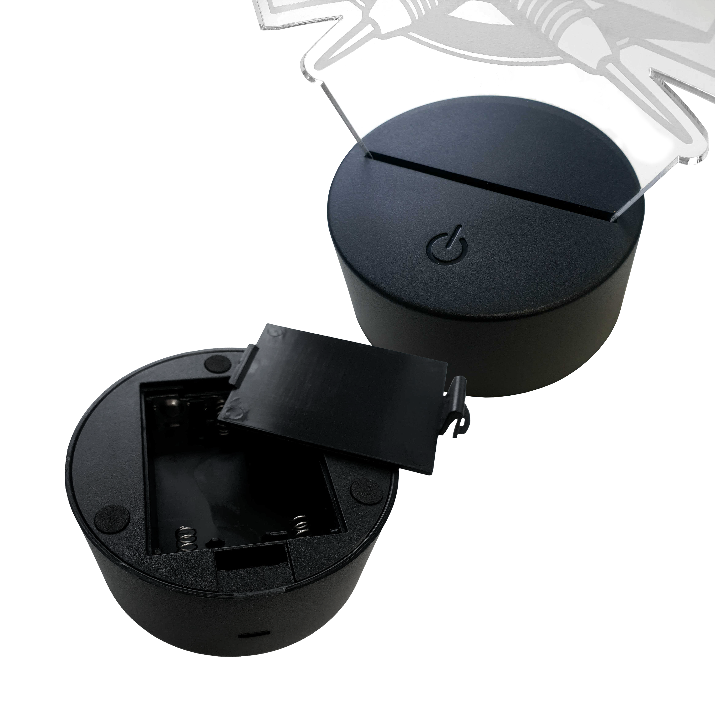 Lámpara de dardo LED de plexiglás con texto personalizado Das Bild zeigt zwei runde LED-Lampen-Sockel aus schwarzem Kunststoff. Einer der Sockel hat ein offenes Batteriefach, der andere ist mit einer Plexiglasplatte bestückt.