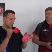 mq1 Zwei Männer stehen nebeneinander in einem Raum. Einer von ihnen hält einen roten Gegenstand und erklärt etwas, während der andere zuschaut.