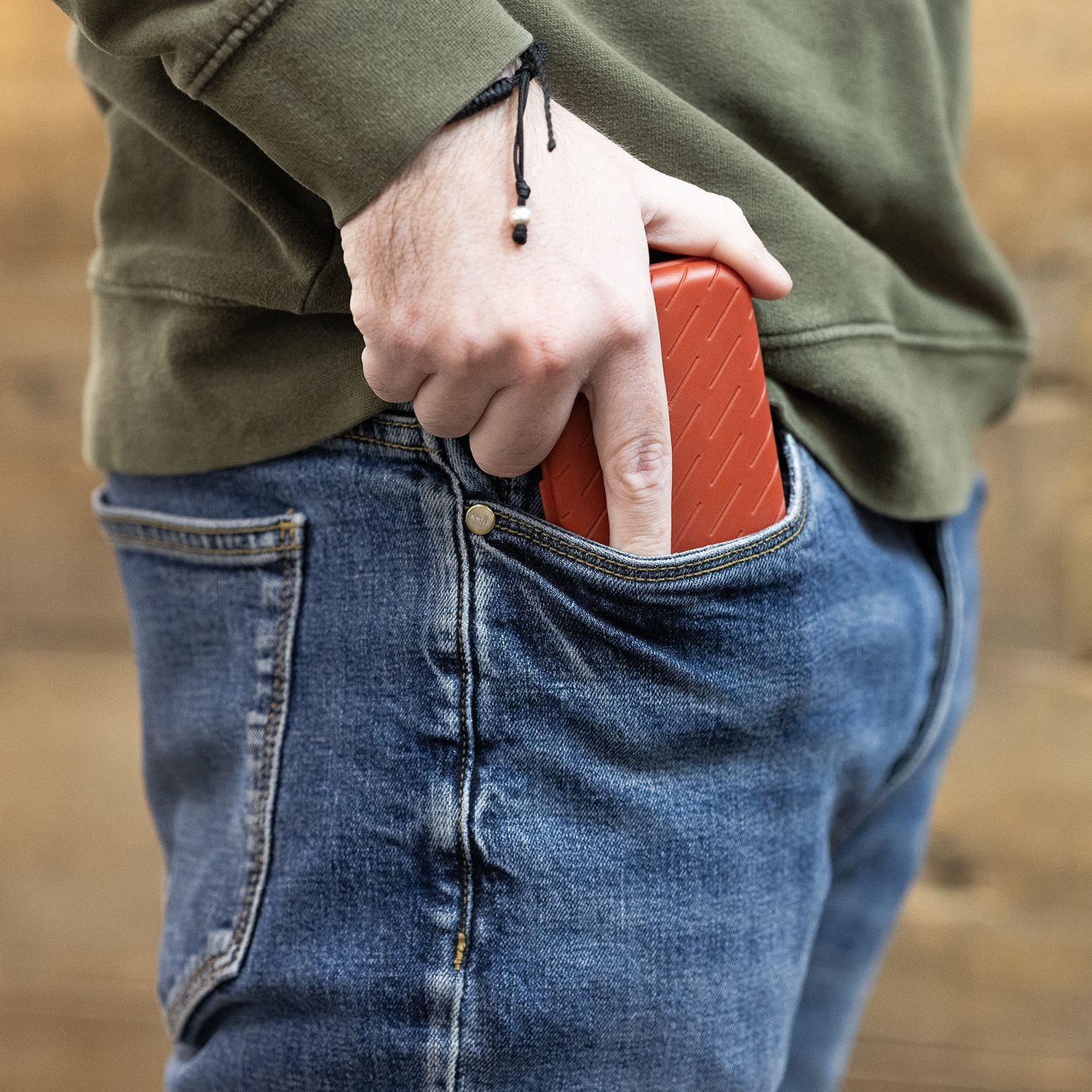 Estuche para dardos Harrows Slimcase Eine Person steckt ein rotes Etui in die Hosentasche. Sie trägt eine blaue Jeans und einen grünen Pullover.