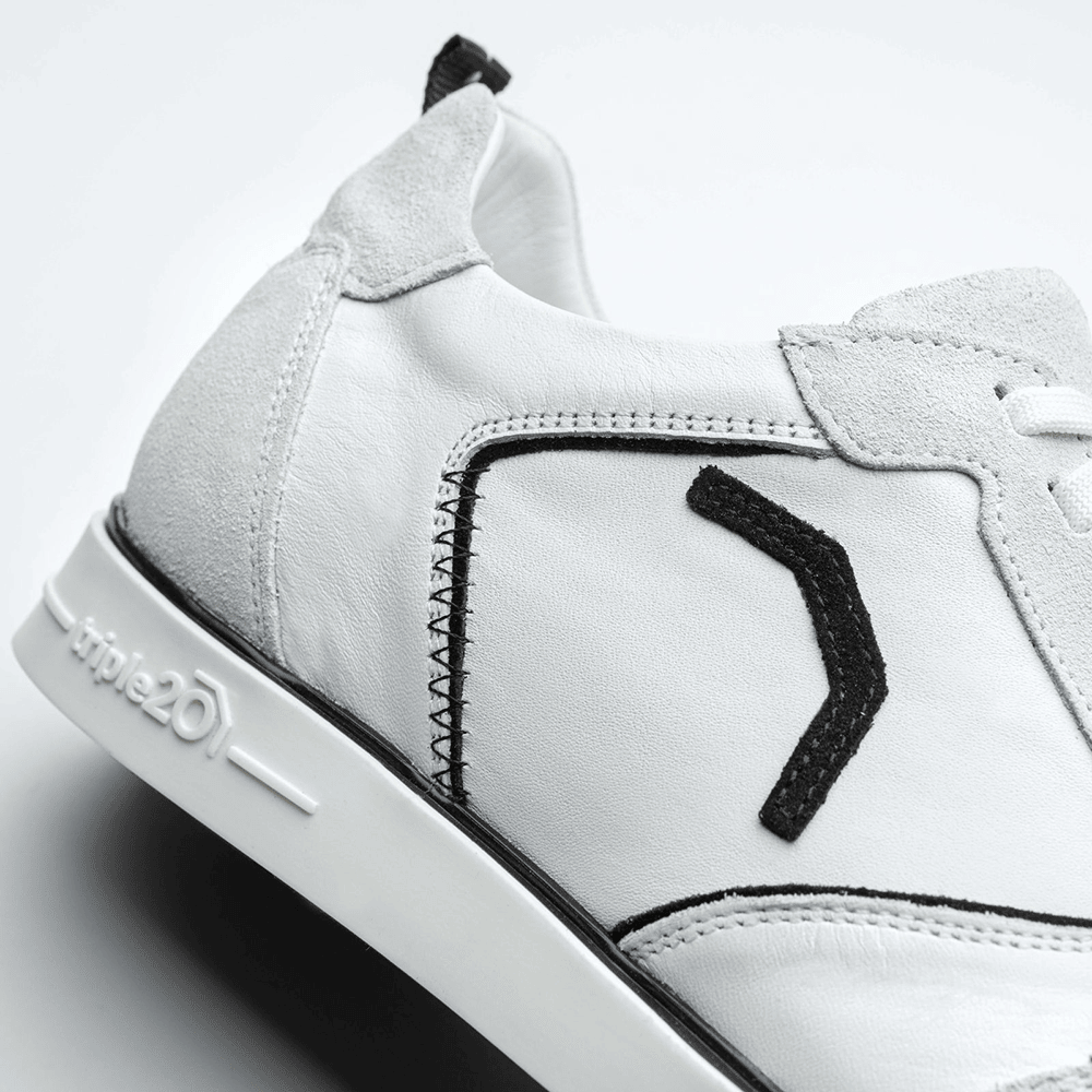 20100002-00_Triple20_Dartschuhe_Leder_Weiss_Schwarz_5 Der „Triple20 Dartschuh Leder – Weiß Schwarz“ ist ein weißer Lederschuh mit schwarzen Akzenten und einer hellen Sohle. Das Logo „triple20“ ist an der Seite der Sohle zu sehen.