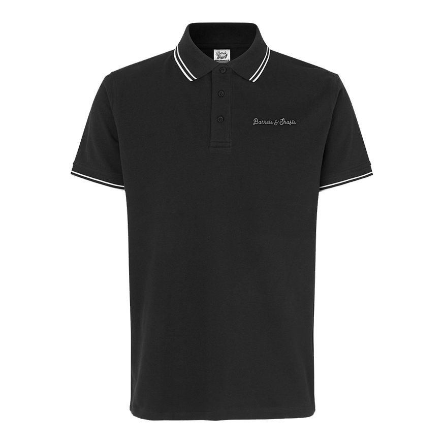 Polo Barriles y Ejes - Negro Das Bild zeigt ein schwarzes Poloshirt mit weißen Akzenten an Kragen und Ärmeln. Auf der Brust ist der Schriftzug "Barrels & Shafts" eingestickt.