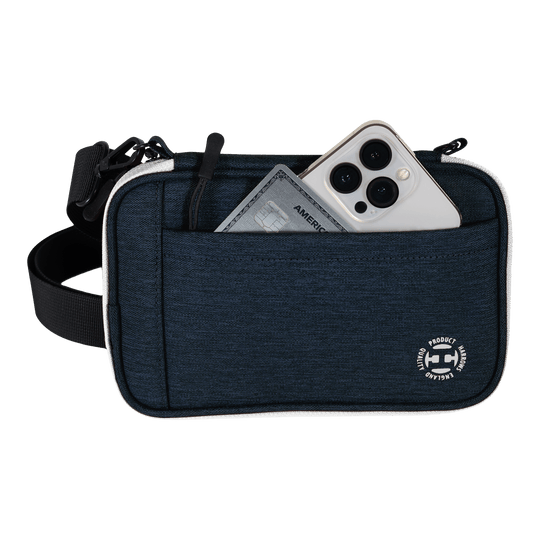 Cartera para dardos Harrows Smart Case XL Eine blaue Tasche mit Vorderfach enthält ein Smartphone und eine Kreditkarte. Am unteren Rand der Tasche befindet sich ein rundes weißes Logo.