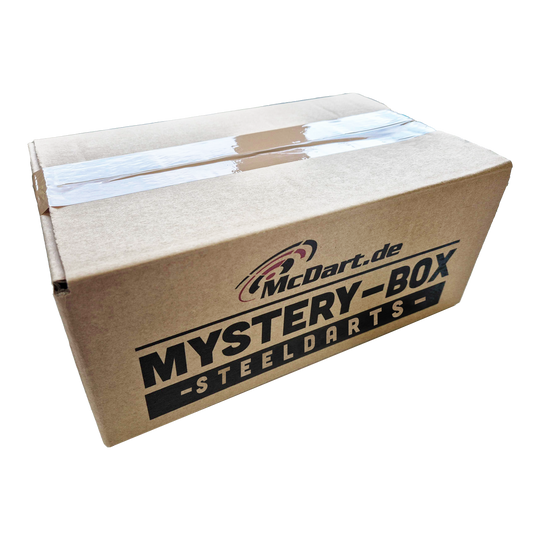Caja misteriosa de McDart - Steeldarts Auf dem Bild ist ein Karton mit der Aufschrift "McDart.de Mystery-Box - Steeldarts" zu sehen. Die Box ist oben mit Klebeband verschlossen.