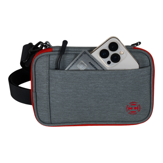 Cartera para dardos Harrows Smart Case XL Das Bild zeigt eine graue Tasche mit rotem Rand und einem schwarzen Gurt. In der Vordertasche stecken ein Smartphone und eine Kreditkarte.