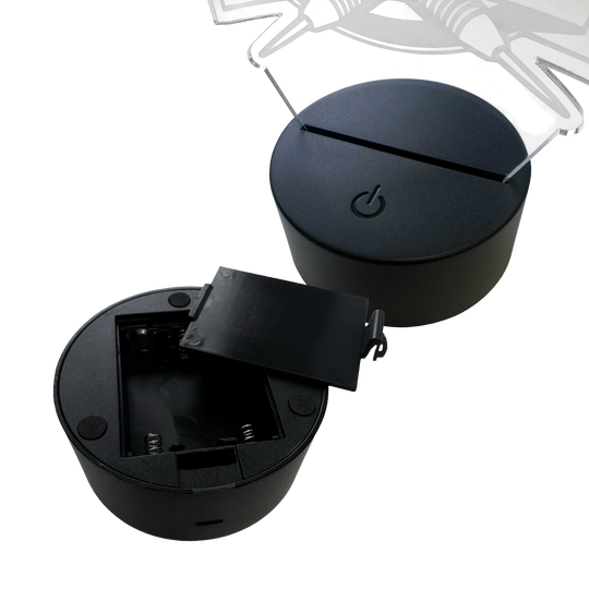 Lámpara de dardo LED de plexiglás con texto personalizado Das Bild zeigt zwei runde LED-Lampen-Sockel aus schwarzem Kunststoff. Einer der Sockel hat ein offenes Batteriefach, der andere ist mit einer Plexiglasplatte bestückt.