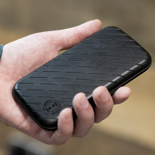Estuche para dardos Harrows Slimcase Eine Person hält eine schwarze, schlanke Darttasche in der Hand. Die Oberfläche der Tasche hat ein dezentes, gerilltes Muster.